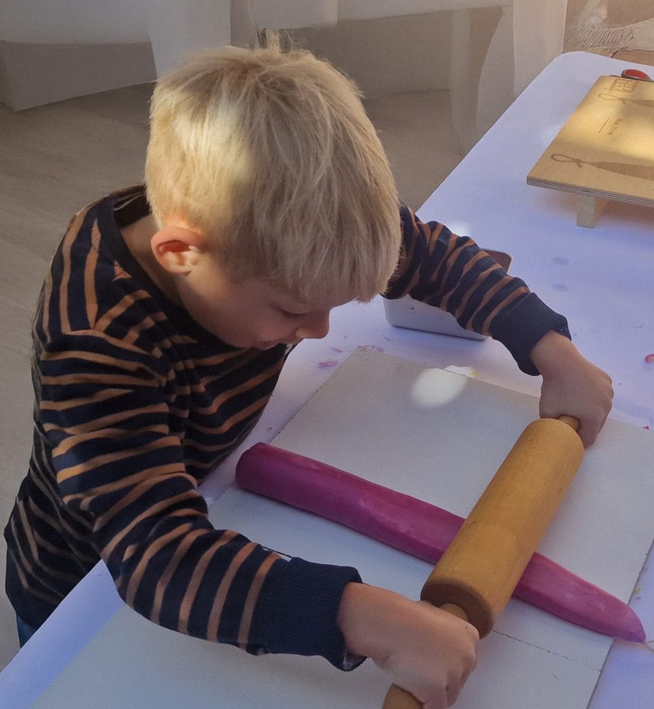 Holzroller zum Teigrollen in der Backstube, Kind beim kreativen Koch-Workshop, Spaß beim Backen mit Teig und Holzrollen, kindgerechtes Backzubehör, handgemachte Aktivität für Kinder.